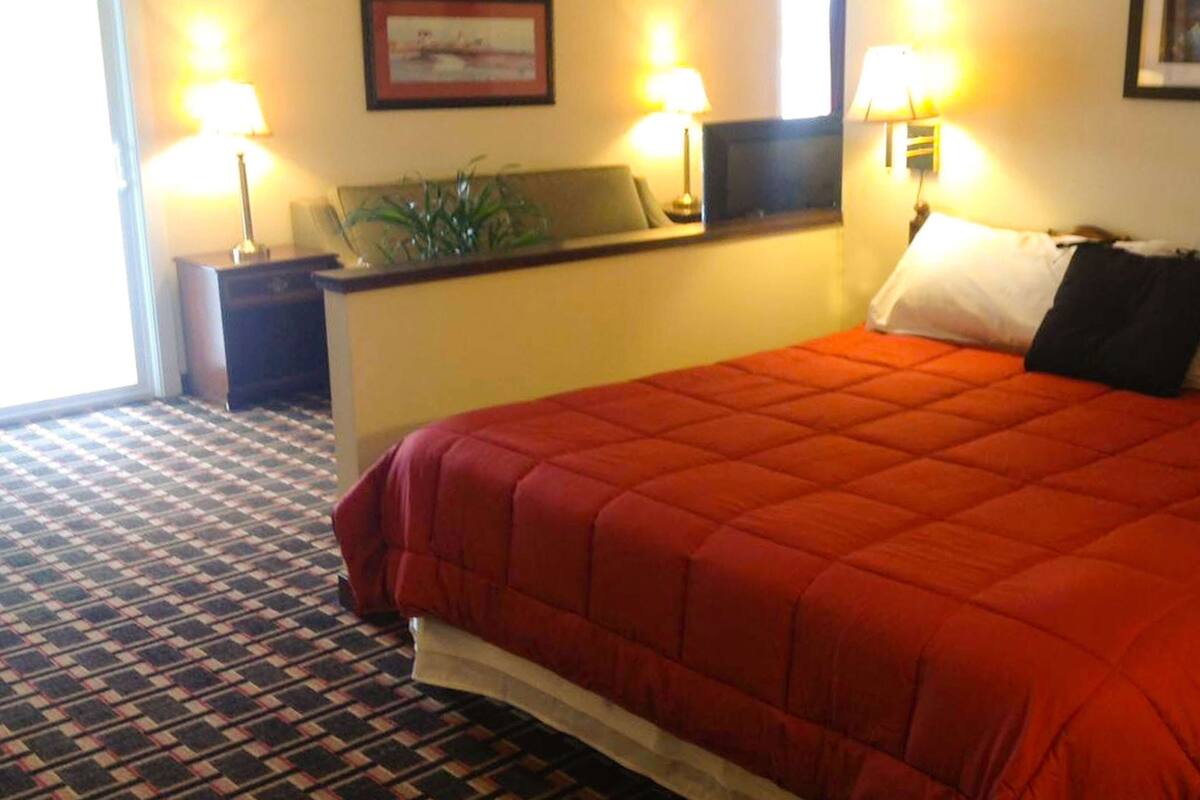 Une chambre d’hôtel avec un grand lit, une table de chevet, un bureau avec une lampe et une fenêtre.