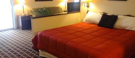 A hotel room with a large bed, a nightstand, a desk with a lamp, and a window.