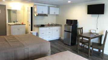 A compact hotel room with a bed, a small kitchenette, a dining area, and a TV mounted on the wall.