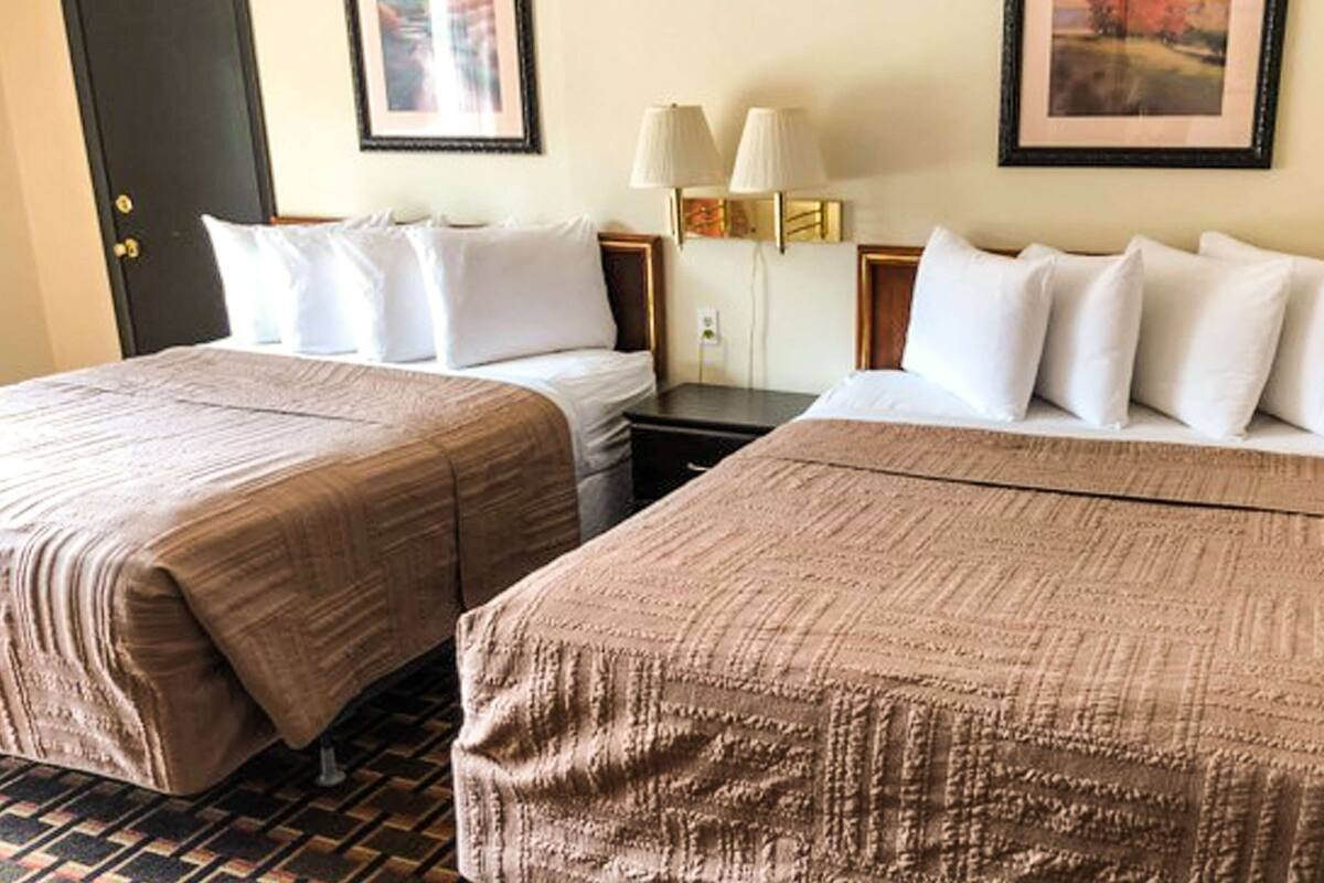 Une chambre d’hôtel avec deux lits, chacun recouvert d’une couverture marron et agrémenté d’oreillers blancs. On y trouve deux tables de chevet avec des lampes et une petite armoire.