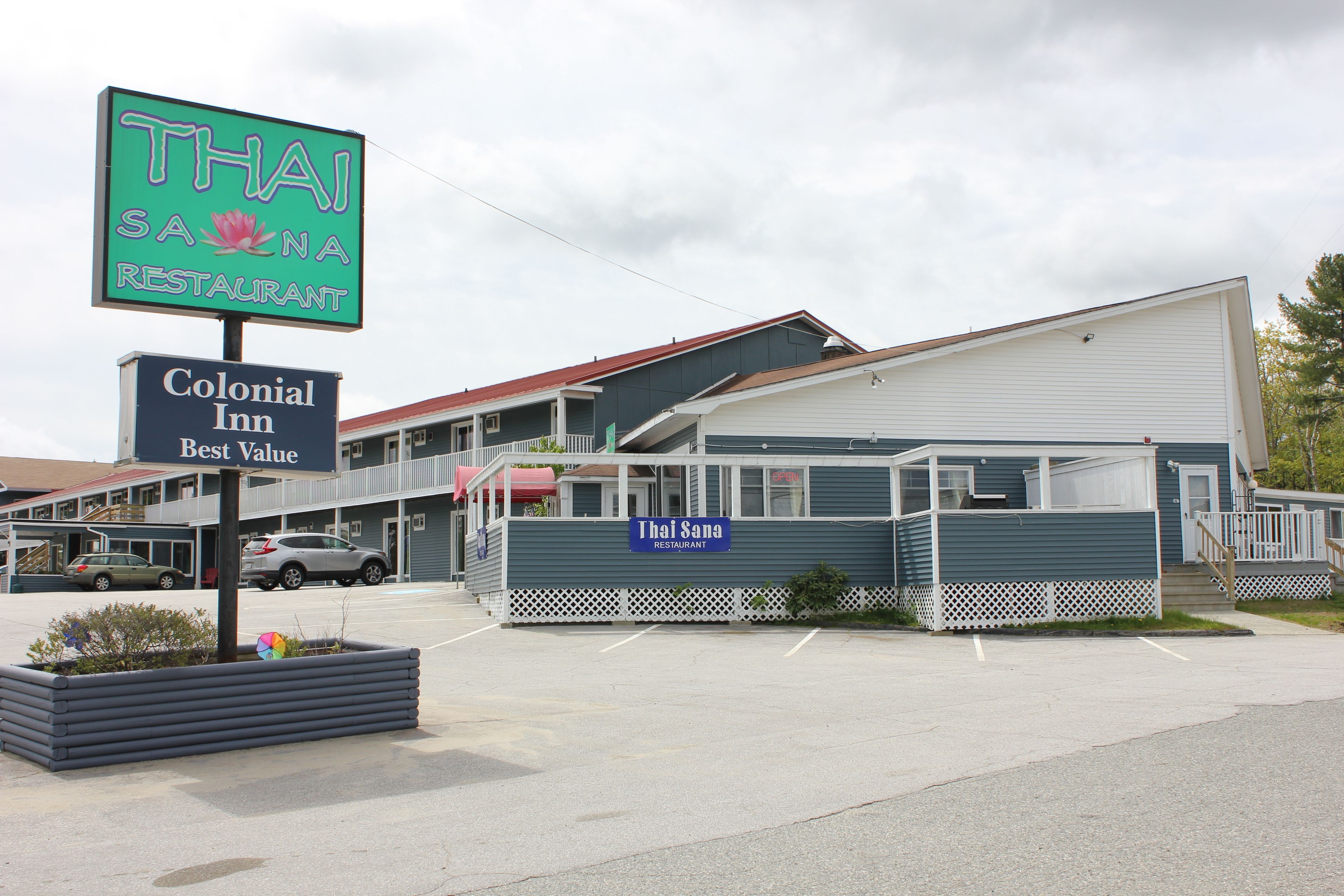 A Thai restaurant with a Colonial Inn sign, a parking lot, and a building with a red roof.