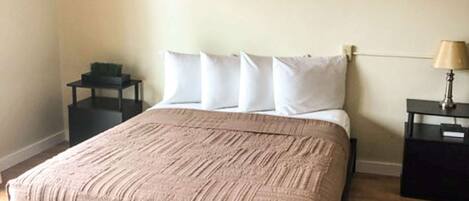 A neatly made bed with a striped blanket, a bedside table with a lamp, and a small nightstand with a plant.