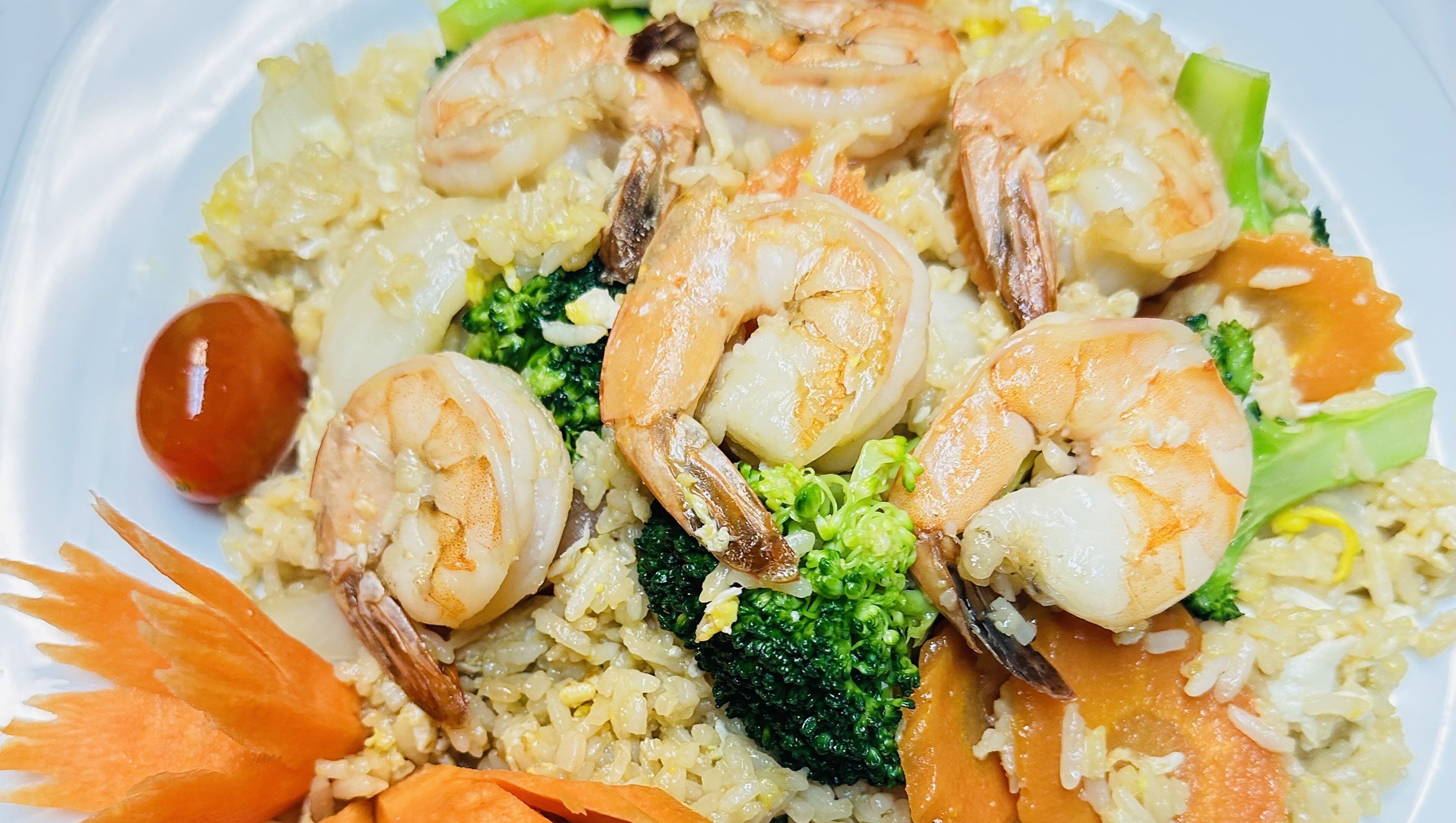 Un piatto di riso fritto con gamberi, broccoli e carote.