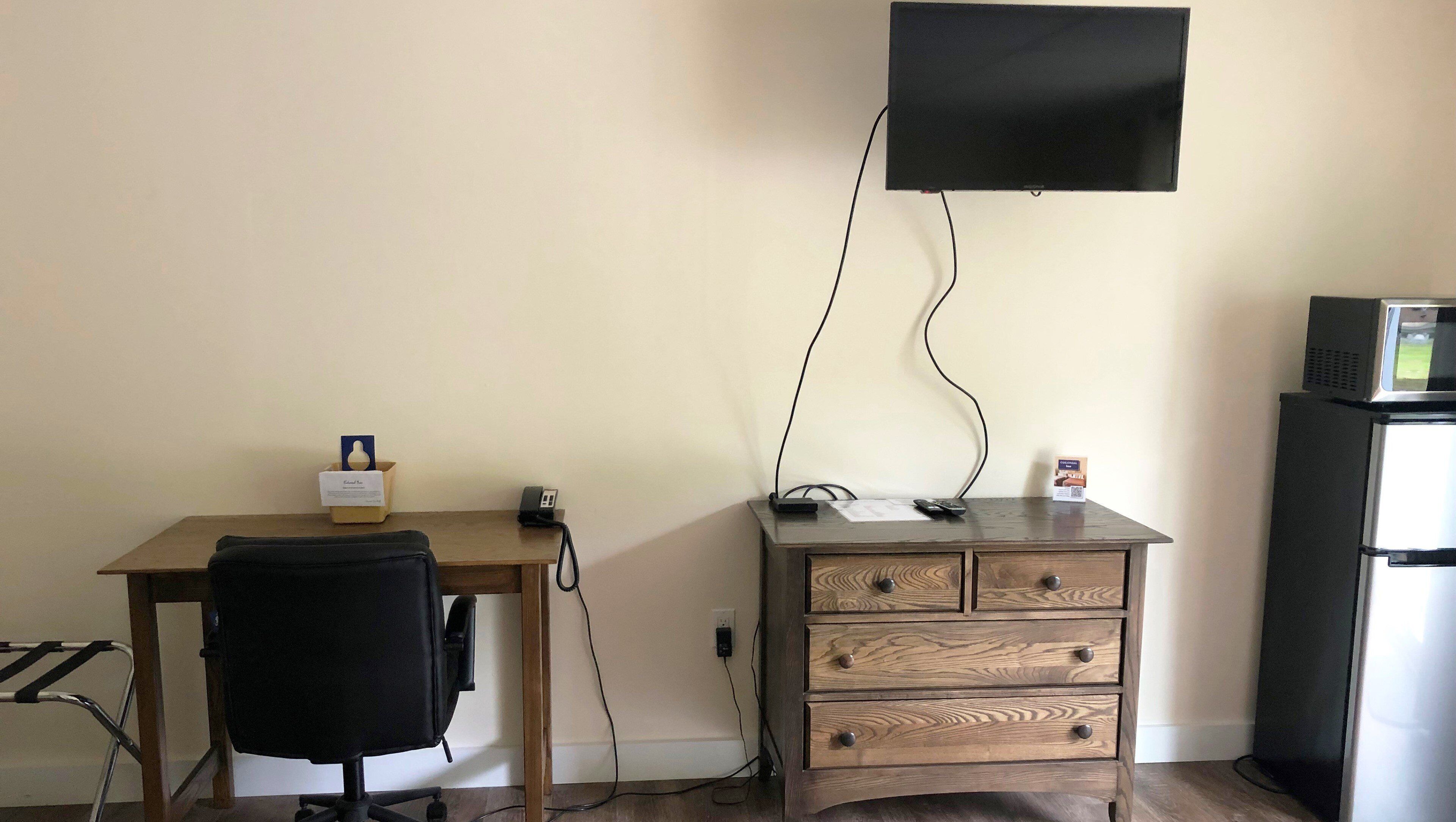 Een kamer met een bureau, stoel, houten dressoir en een flatscreen televisie aan de muur.