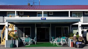 A building with a sign labeled "OFFICE" above the entrance, a covered outdoor seating area with chairs and tables, and a "WELCOME" sign on a trash can.