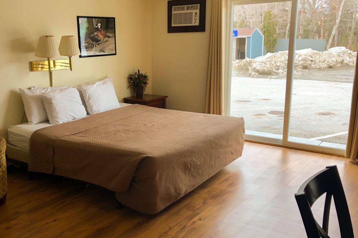 Une chambre d’hôtel avec un lit, une chaise, une lampe, un tableau au mur et une fenêtre donnant sur l’extérieur.