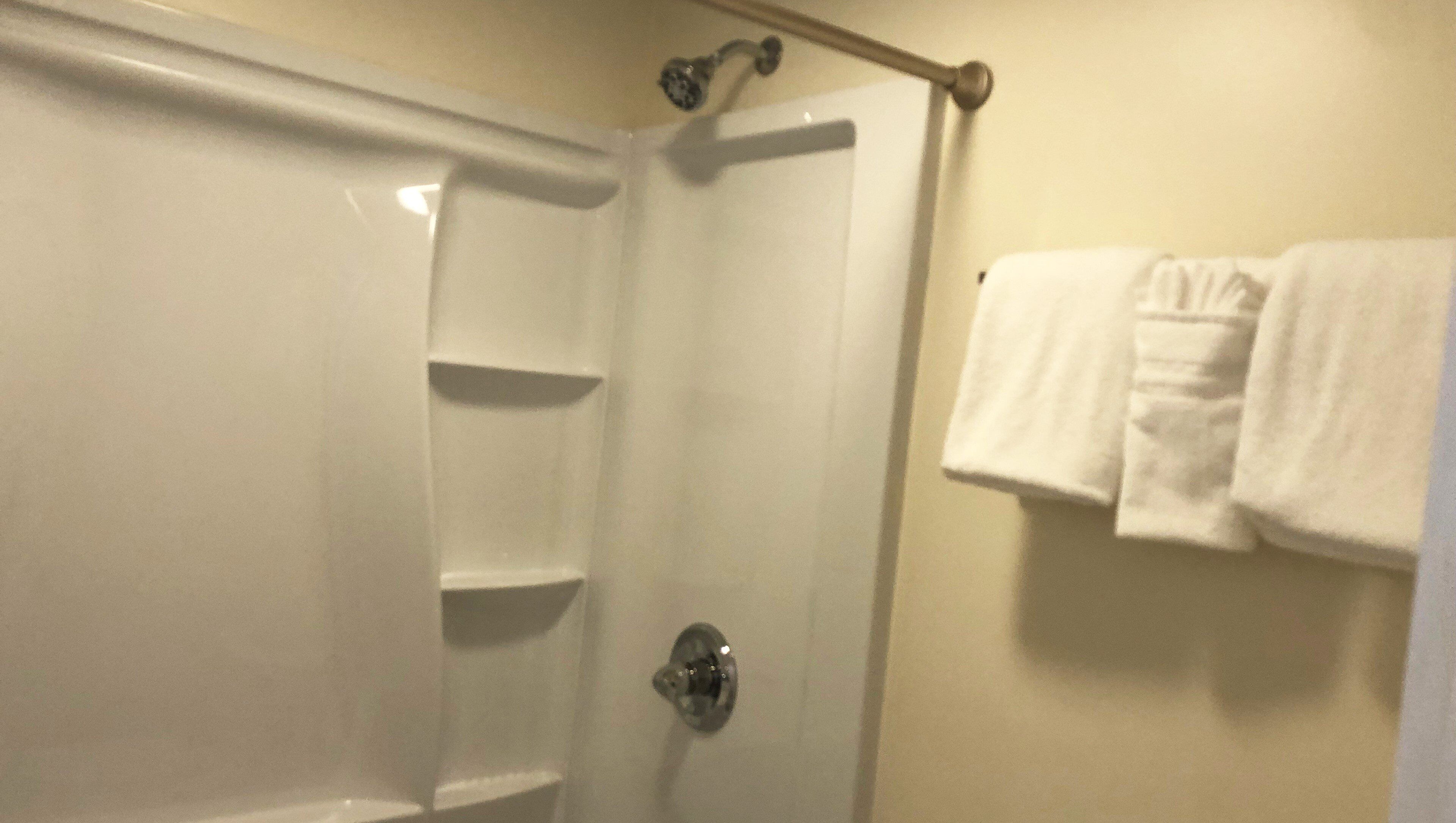 A bathroom with a shower, a towel rack with towels, and a door.