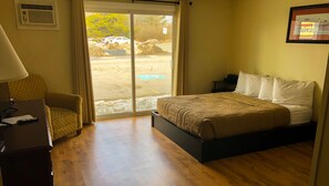A hotel room with a bed, a chair, a desk with a lamp, and a window with a view of the outside.