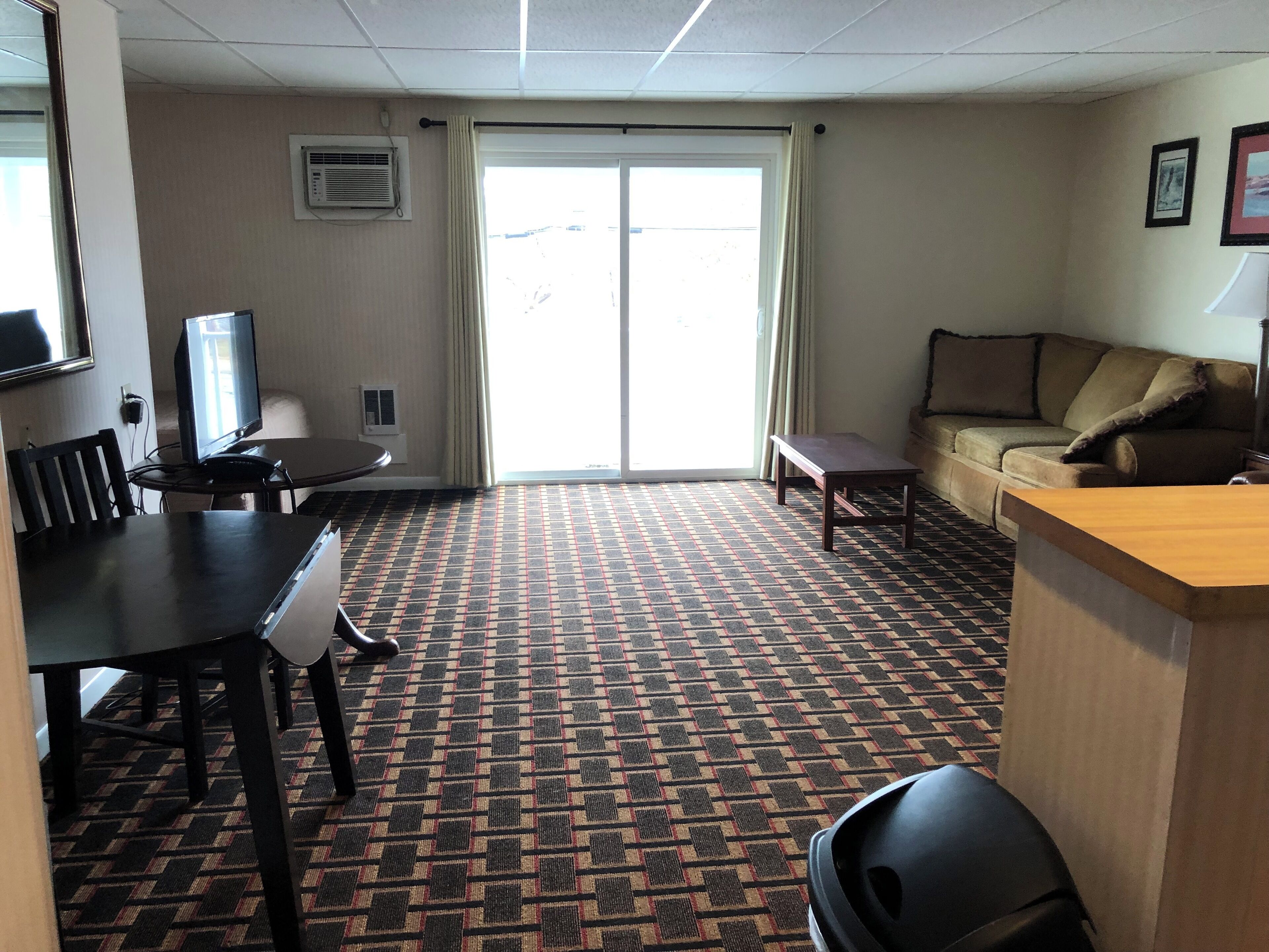 Hotelkamer met een eethoek, een bank, een televisie en een kamerbreed tapijt met dessin.