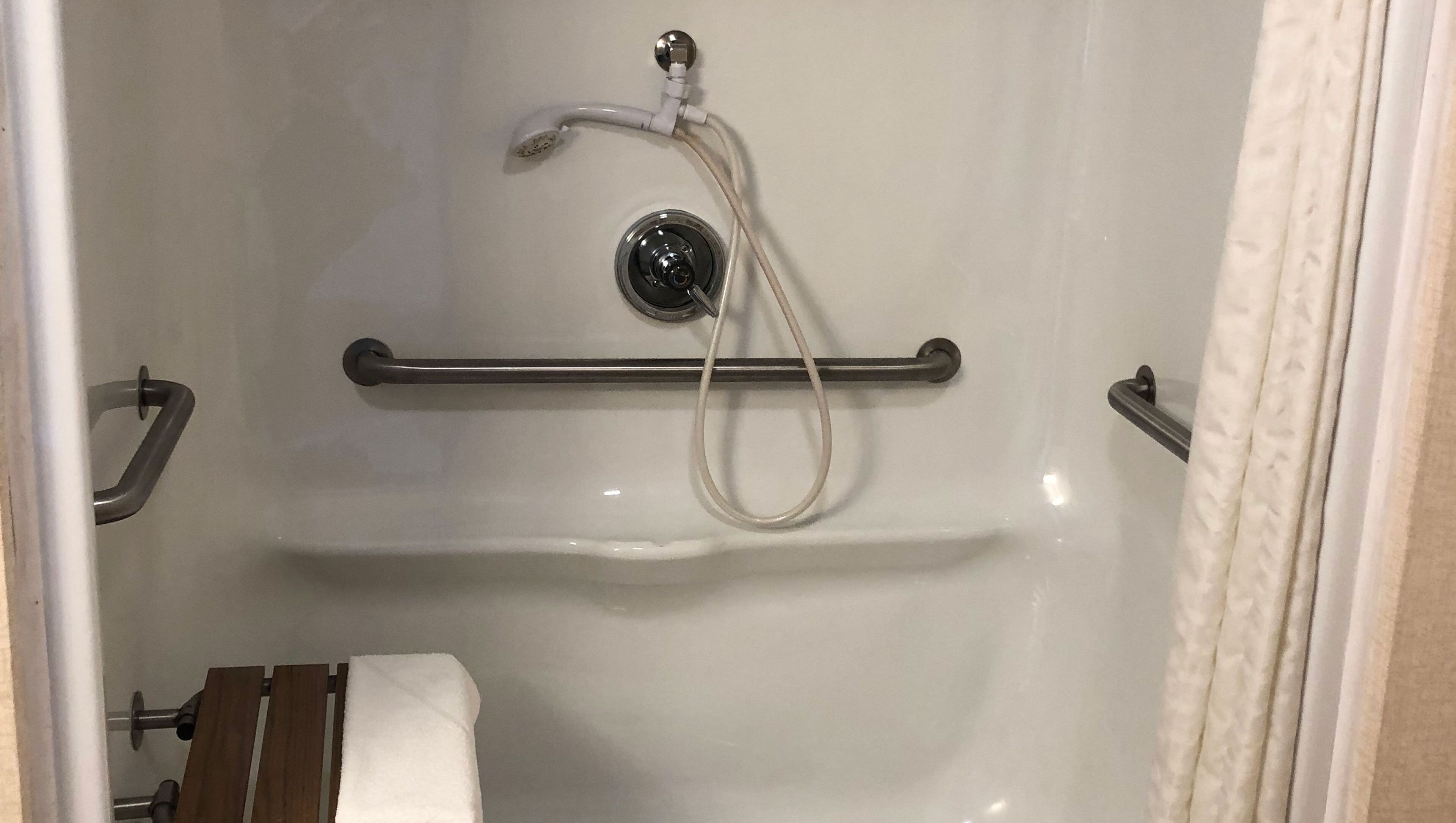 A shower with a handheld showerhead, a grab bar, and a towel rack.