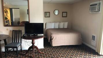 A hotel room with a bed, a television on a wooden table, a mirror, and a patterned carpet.