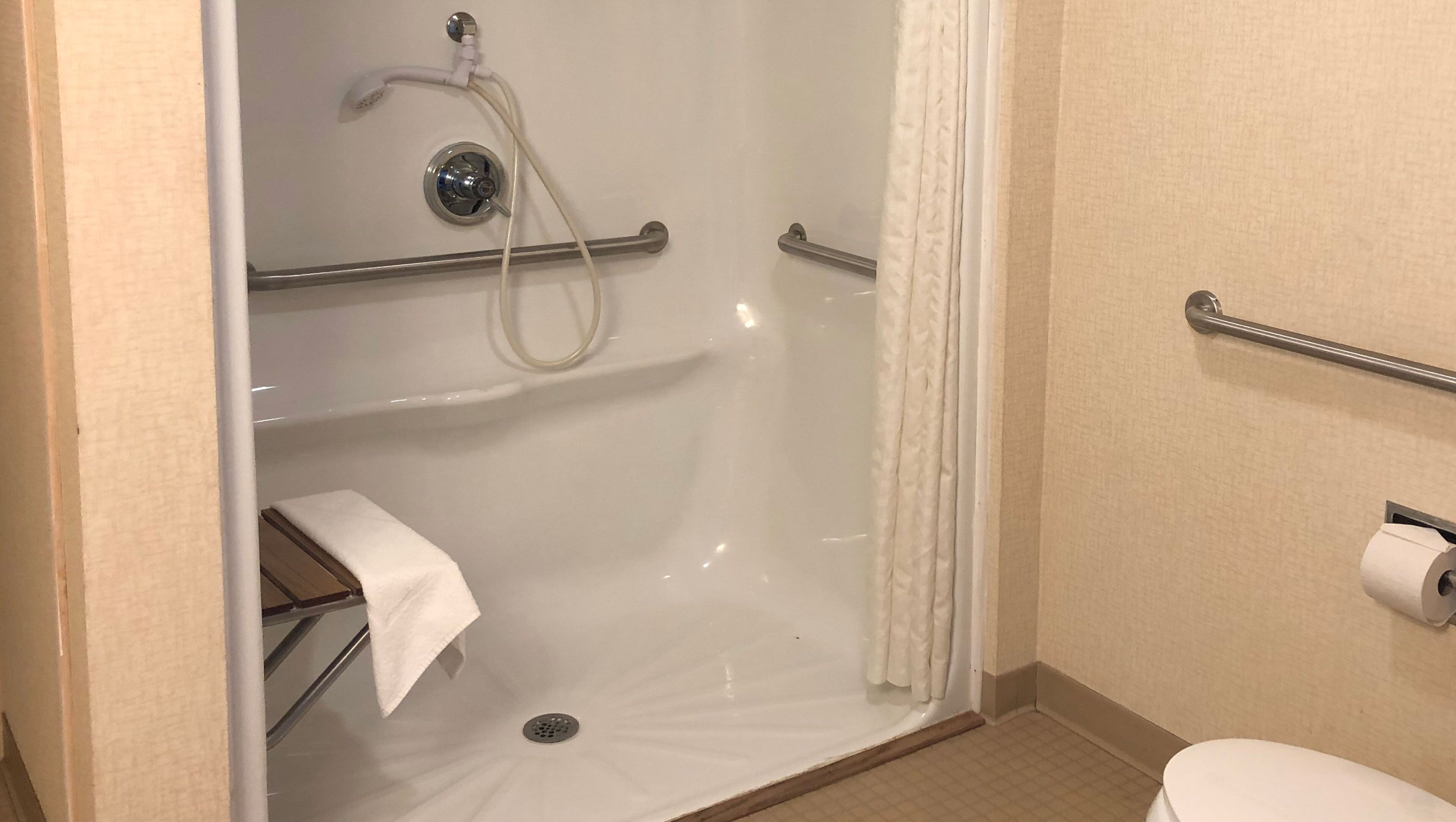 Un espace douche équipé d’une barre d’appui, d’un porte-serviettes et de toilettes avec un distributeur de serviettes en papier.