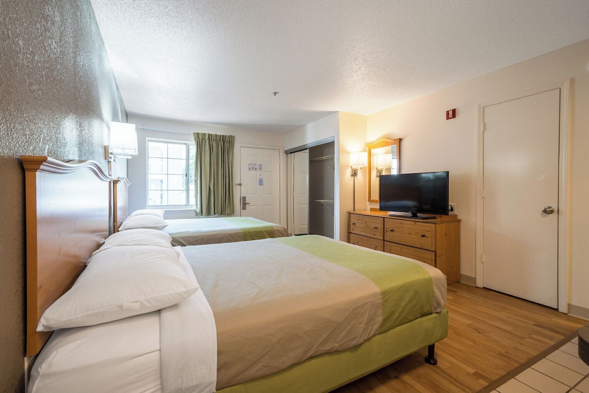 A hotel room with two beds, a television, a dresser, and a window with curtains.