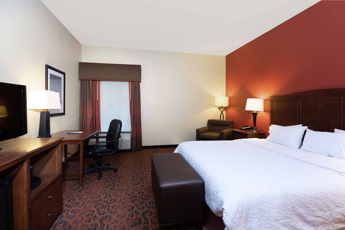 A hotel room with a bed, a desk, a chair, a TV, and two lamps.