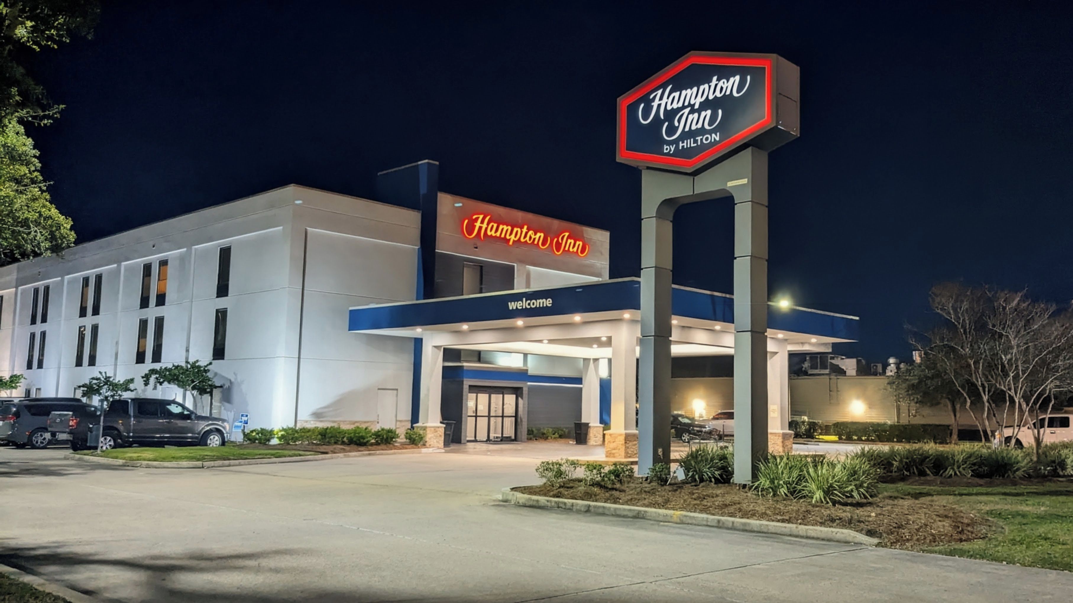 A Hampton Inn by Hilton hotel with a prominent neon sign, a welcoming entrance, and a parking lot.