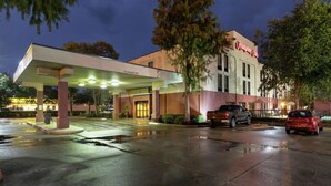 A hotel with a covered parking area, a sign indicating 'Clearance 10ft', and a 'Hampton Inn' sign.