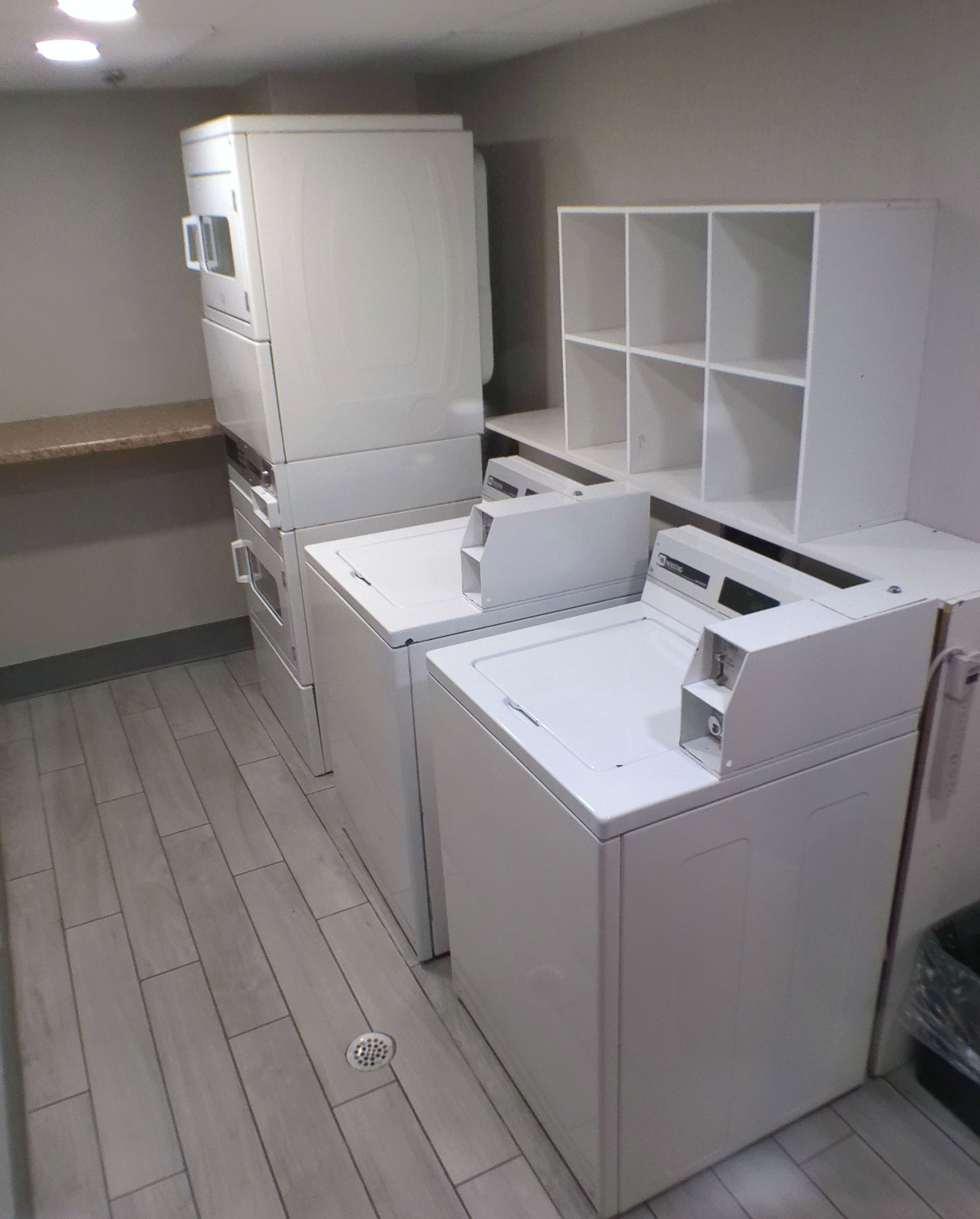 A laundry room with stacked washing machines and dryers, a metal sink, and a tiled floor.