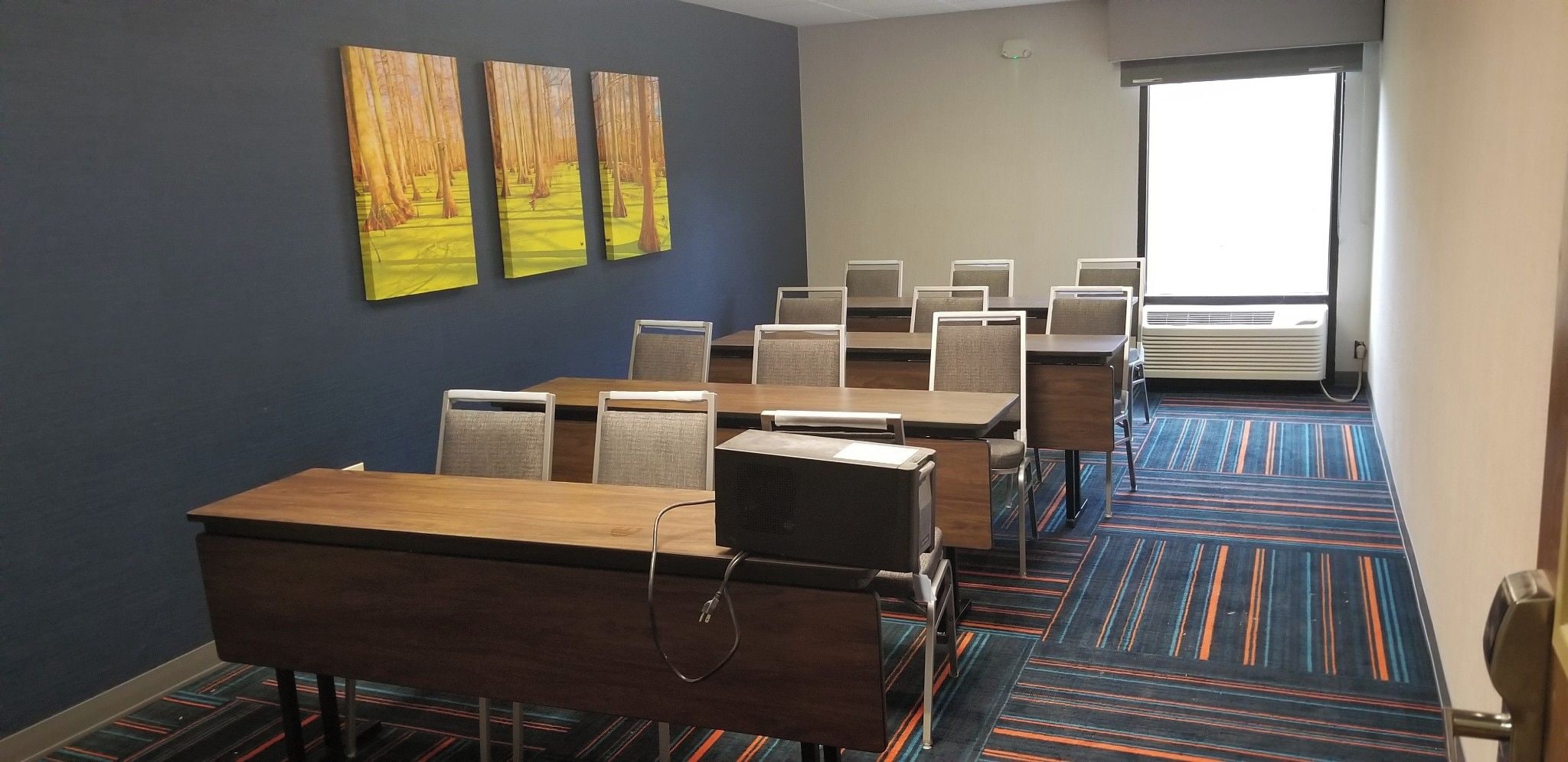 A conference room with a long table, multiple chairs, a projector, and a large window with blinds.