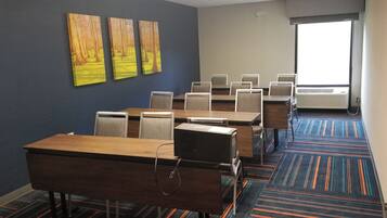 A conference room with a long table, multiple chairs, a projector, and a large window with blinds.