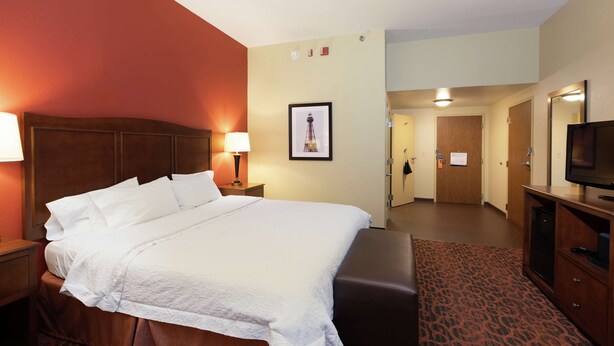 A hotel room with a large bed, a wooden headboard, a desk with a lamp, a television, and a framed picture on the wall.