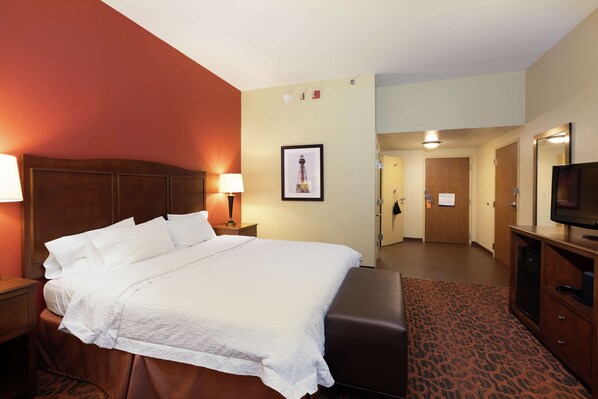 A hotel room with a large bed, a wooden headboard, a desk with a lamp, a television, and a framed picture on the wall. - Hampton Inn Houma (Houma)