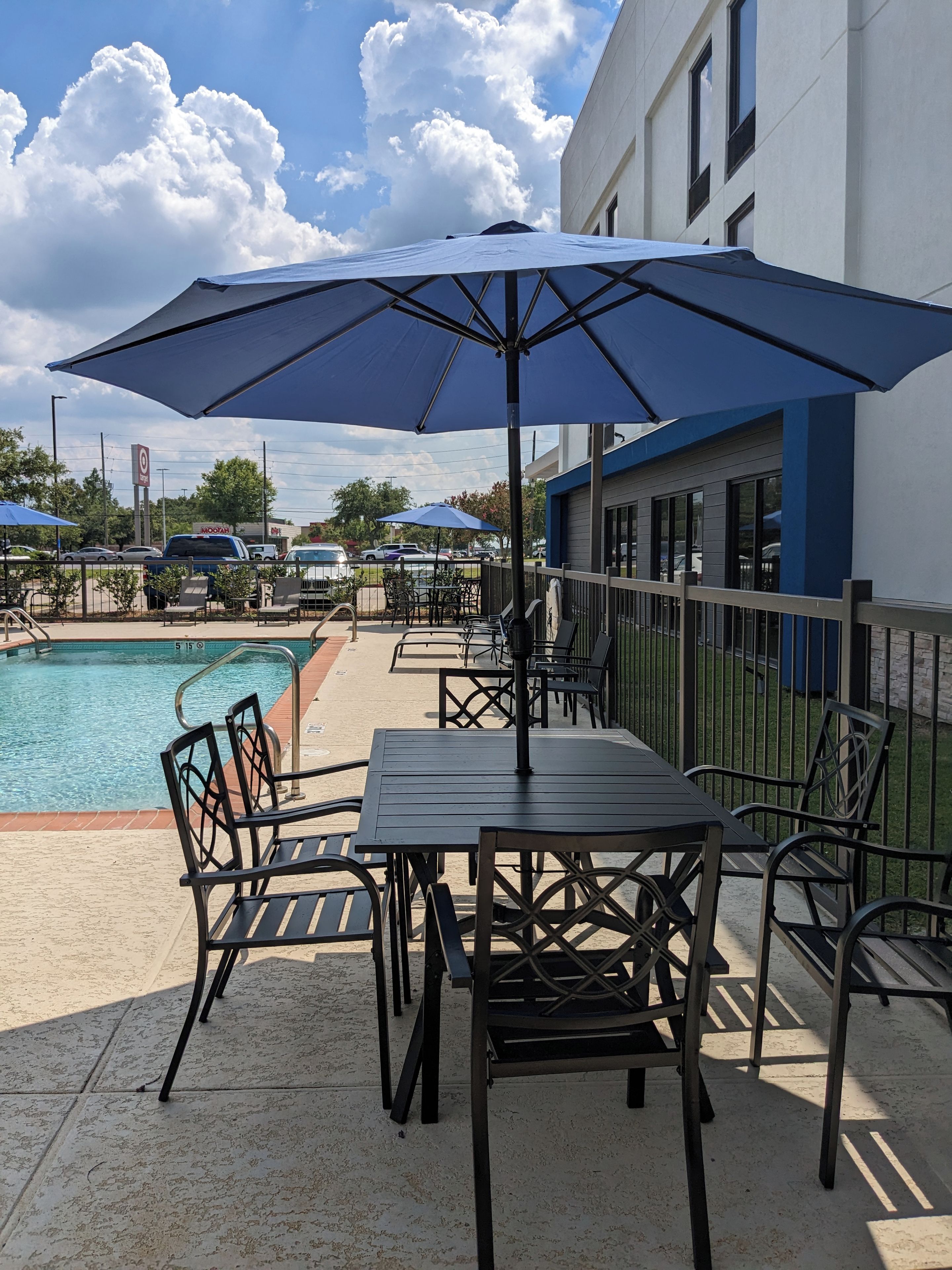 An outdoor seating area with a pool, tables, and chairs, under a large umbrella.