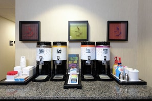 A coffee station with multiple dispensers, disposable cups, and a sign that reads "Instant Human Just Add Coffee."
