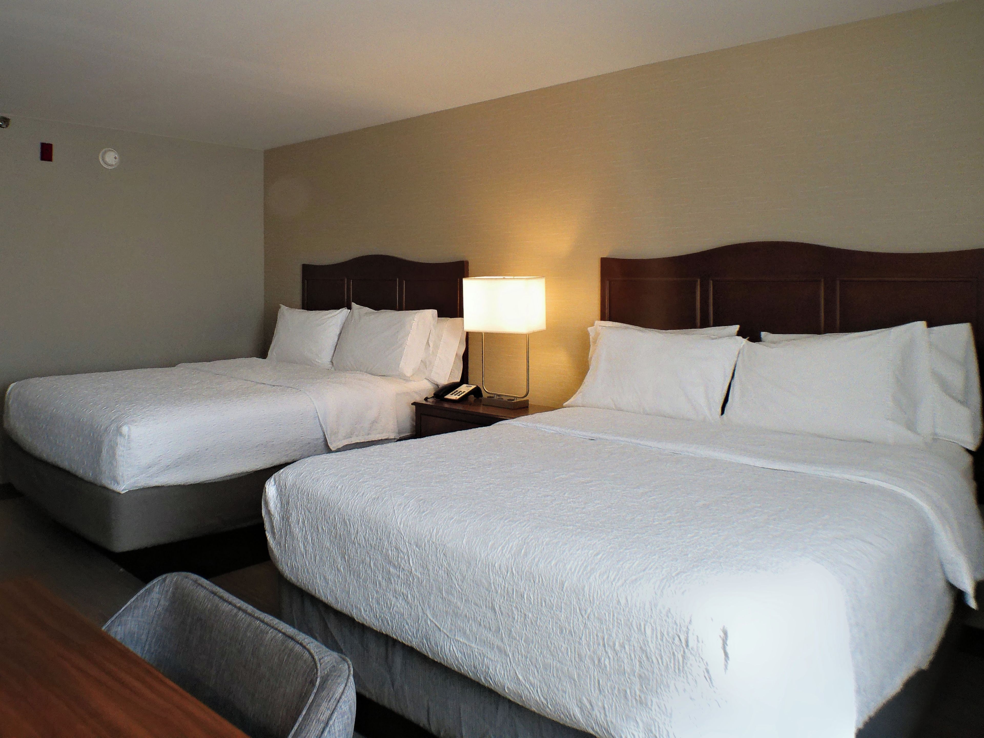 A hotel room with two beds, a nightstand with a lamp, and a small seating area.