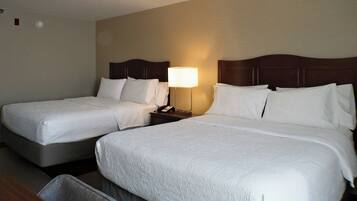 A hotel room with two beds, a nightstand with a lamp, and a small seating area.