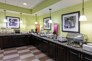 A hotel kitchen with a checkered floor, dark cabinets, and various appliances like a coffee maker and toaster.