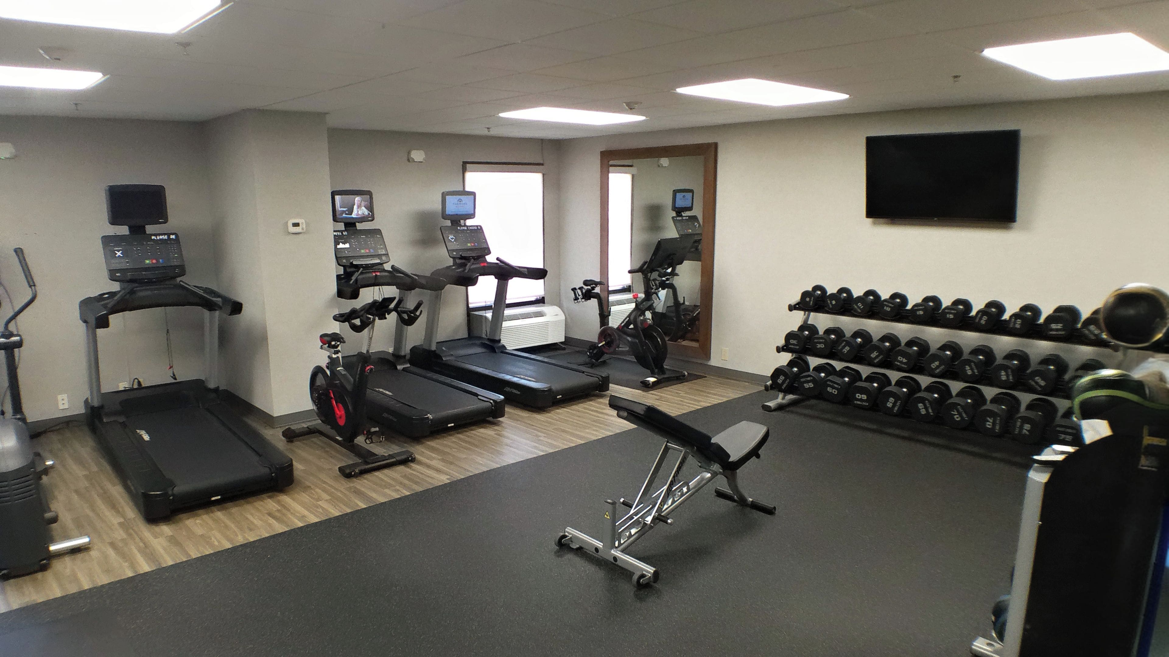 A gym with treadmills, an elliptical, a stationary bike, and a bench. There are also dumbbells and a weight rack.