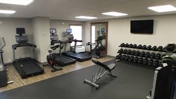 A gym with treadmills, an elliptical, a stationary bike, and a bench. There are also dumbbells and a weight rack.