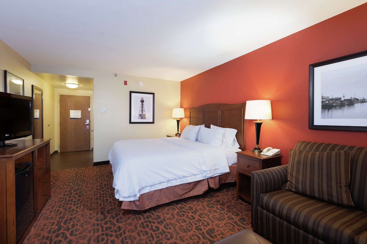 A hotel room with a bed, a sofa, a TV, a desk, and a lamp.