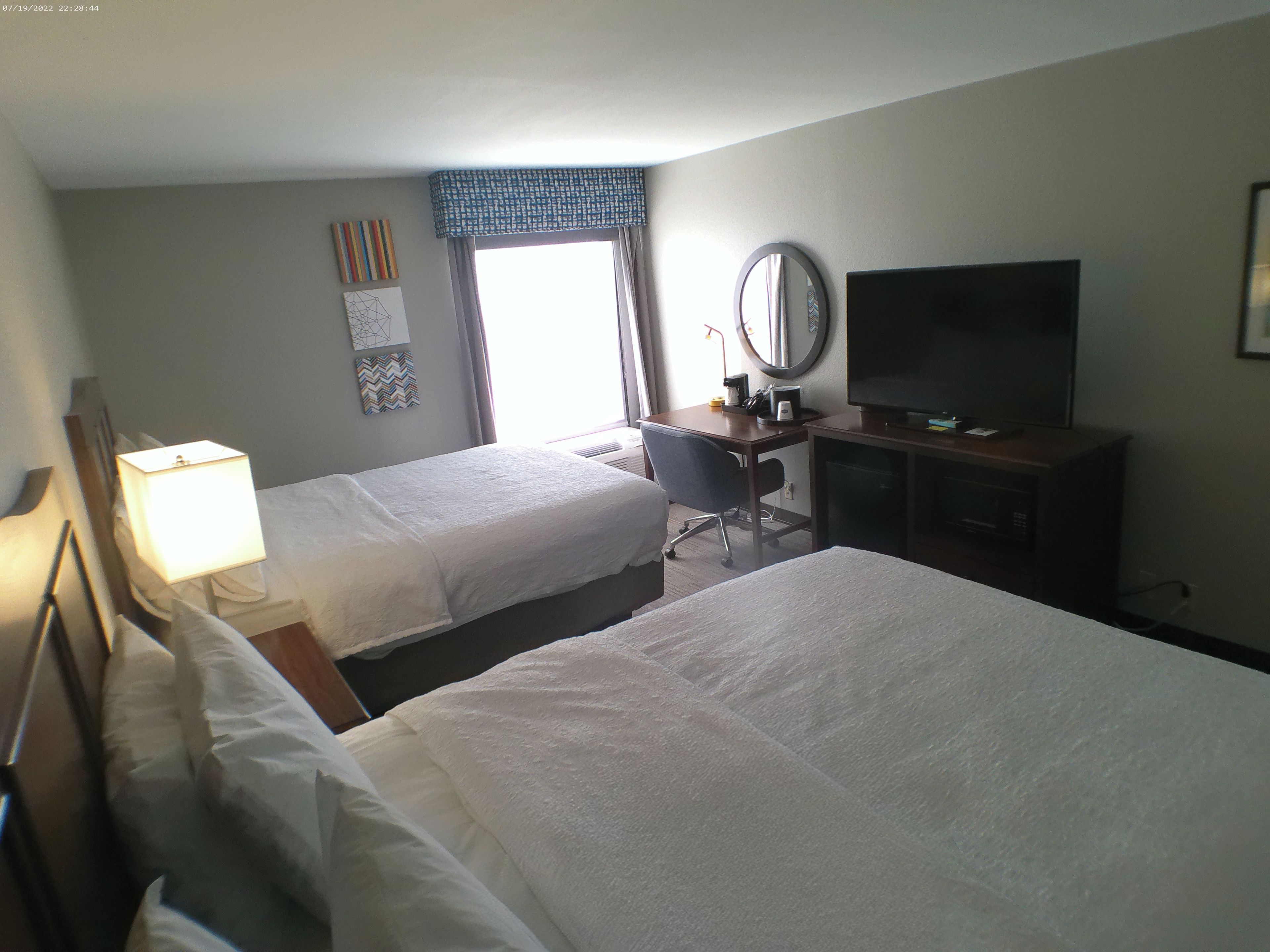 A hotel room with two beds, a desk with a chair, a television, and a window with curtains.