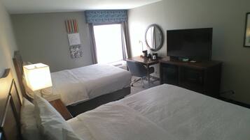 A hotel room with two beds, a desk with a chair, a television, and a window with curtains.