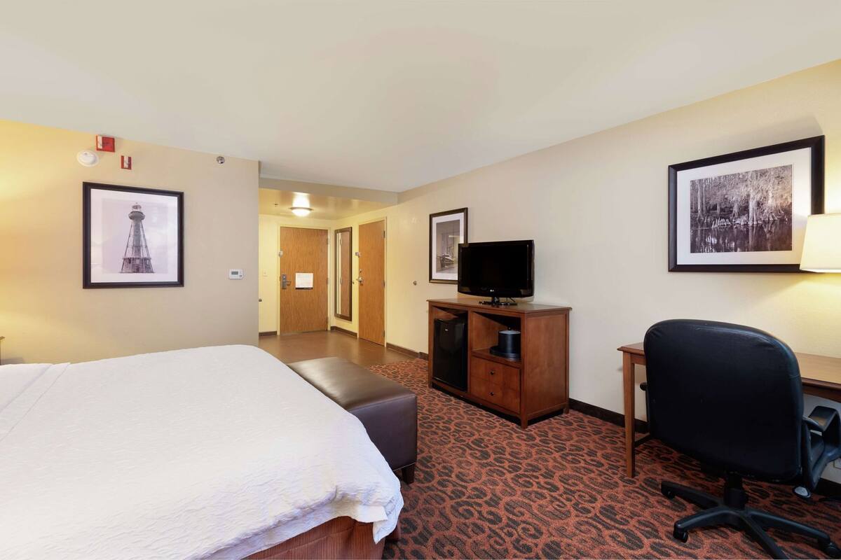 A hotel room with a bed, a desk with a television, a chair, and a carpeted floor.