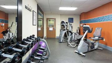 A gym with various exercise equipment including dumbbells, a stationary bike, and an elliptical trainer.