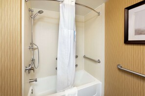 A corner shower with a white curtain, grab bars, and a framed picture on the wall.