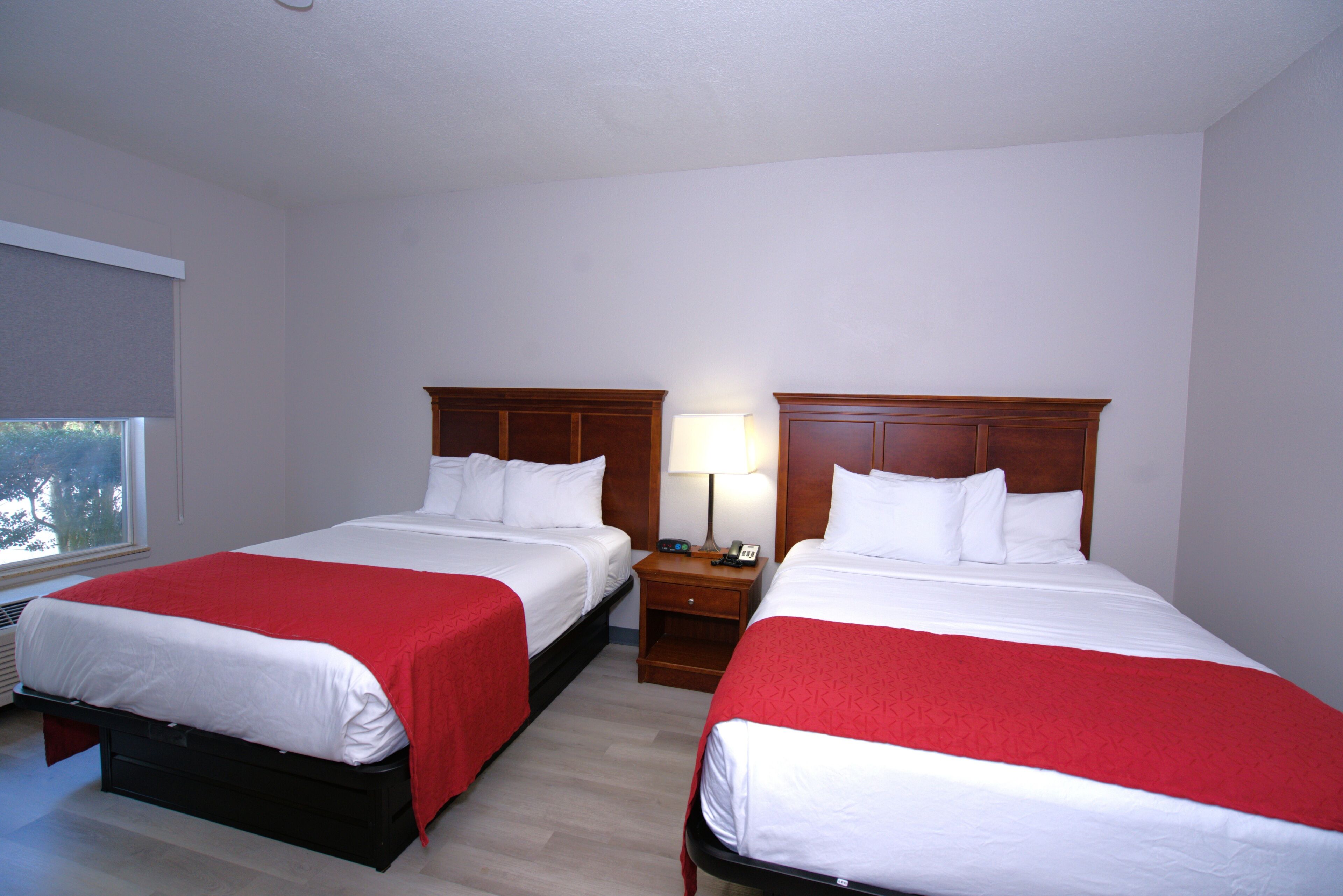 Quarto de hotel com duas camas, uma mesa de cabeceira com abajur e uma janela.