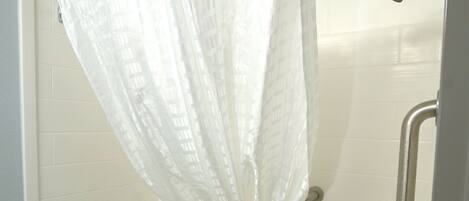 A bathroom with a bathtub, a shower curtain, and a grab bar.