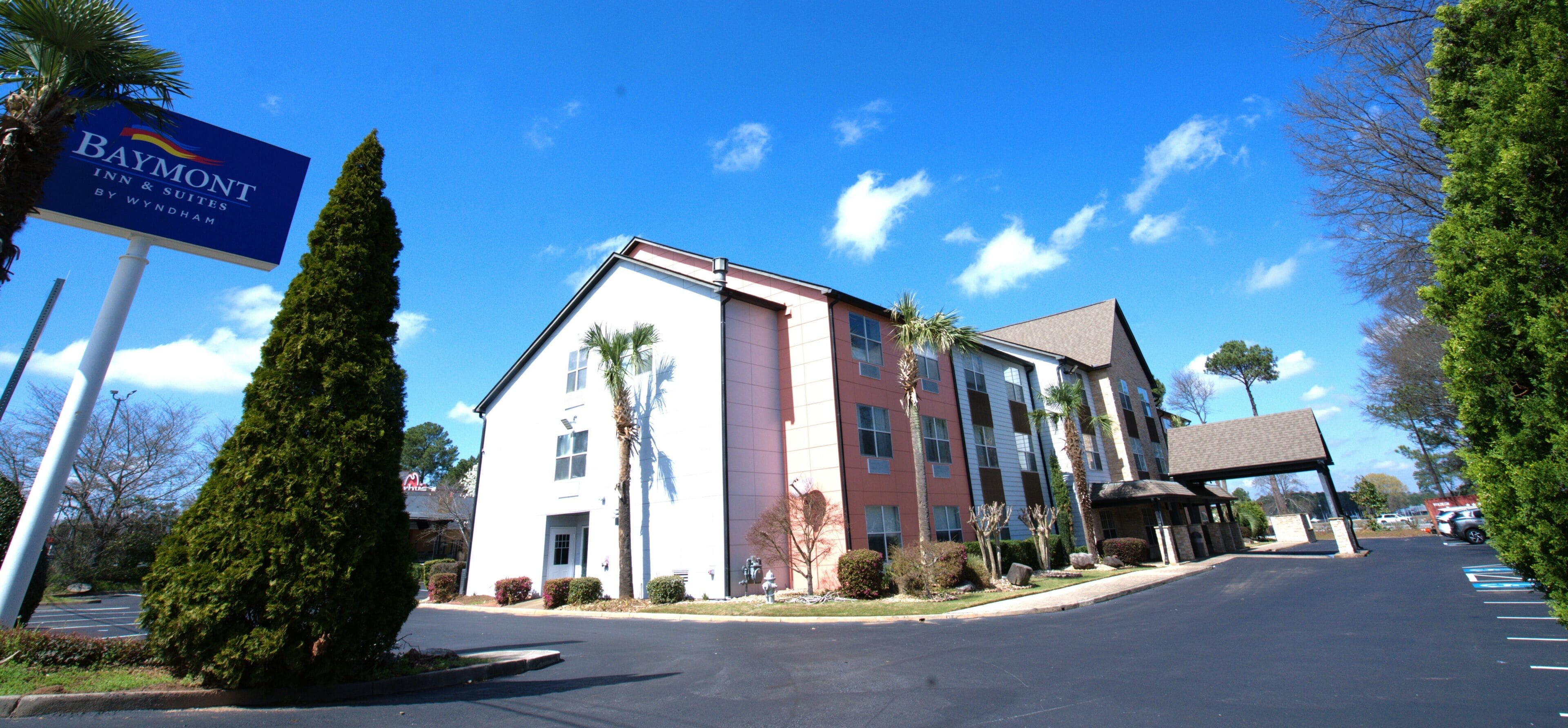 A multi-story hotel with a prominent sign, a parking lot, and a clear sky.