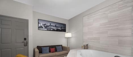 A modern bathroom with a freestanding bathtub, a sofa, and a cityscape artwork on the wall.