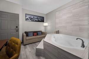 A modern bathroom with a freestanding bathtub, a sofa, and a cityscape artwork on the wall.