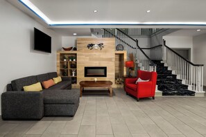 A modern living room with a grey sectional sofa, a red armchair, a wooden entertainment unit, and a staircase with black railings. - Baymont Inn & Suites by Wyndham Morrow/Atlanta I-75 South (Morrow)