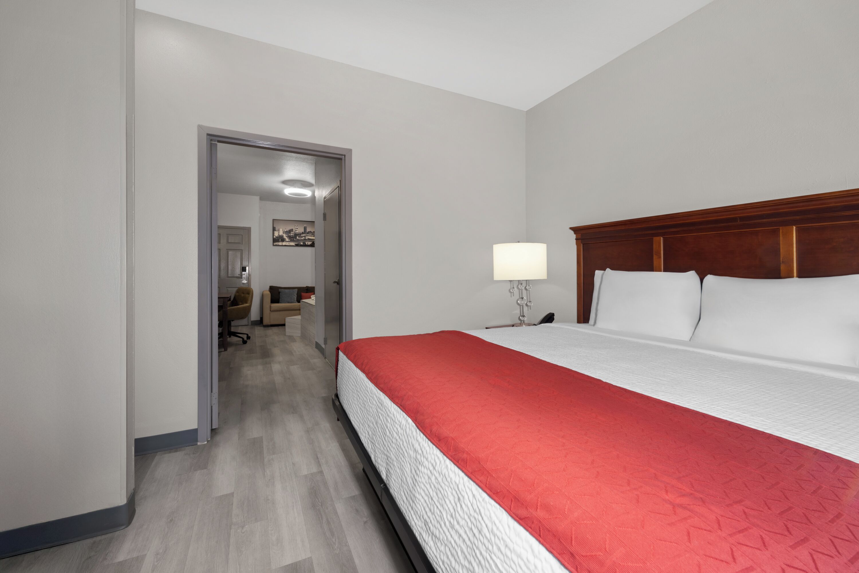 A hotel room with a bed, a nightstand, a lamp, and a door leading to another room.