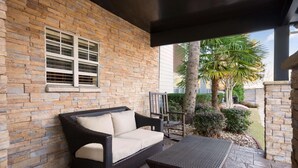 A covered patio with a wicker sofa and table, stone walls, and a palm tree. - Baymont Inn & Suites by Wyndham Morrow/Atlanta I-75 South (Morrow)