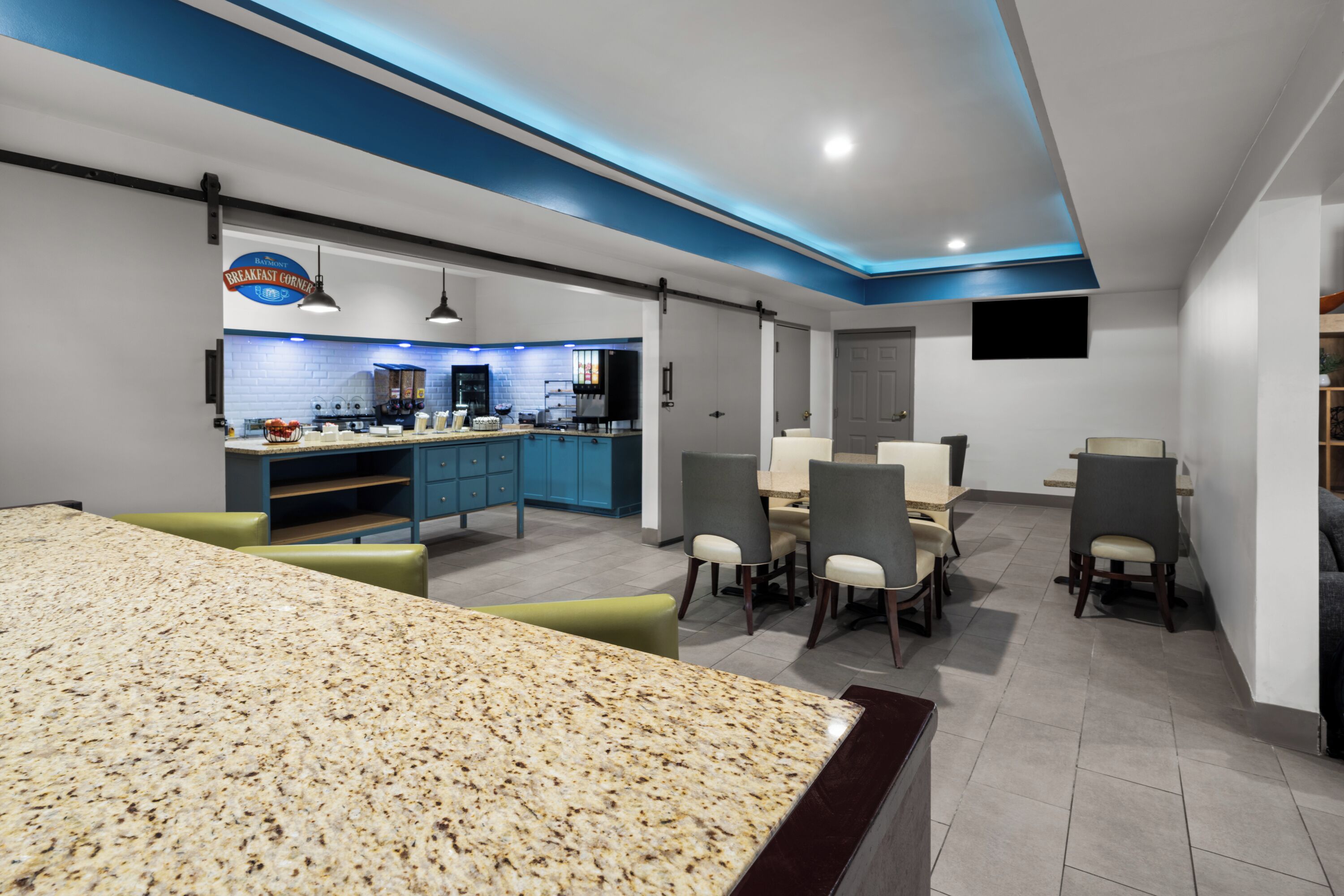 A modern kitchen with a breakfast bar, dining area with chairs, and a TV mounted on the wall.