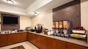 A hotel kitchen with wooden cabinets, a flat-screen TV, a coffee station, and a fruit display. - Baymont Inn & Suites by Wyndham Morrow/Atlanta I-75 South (Morrow)