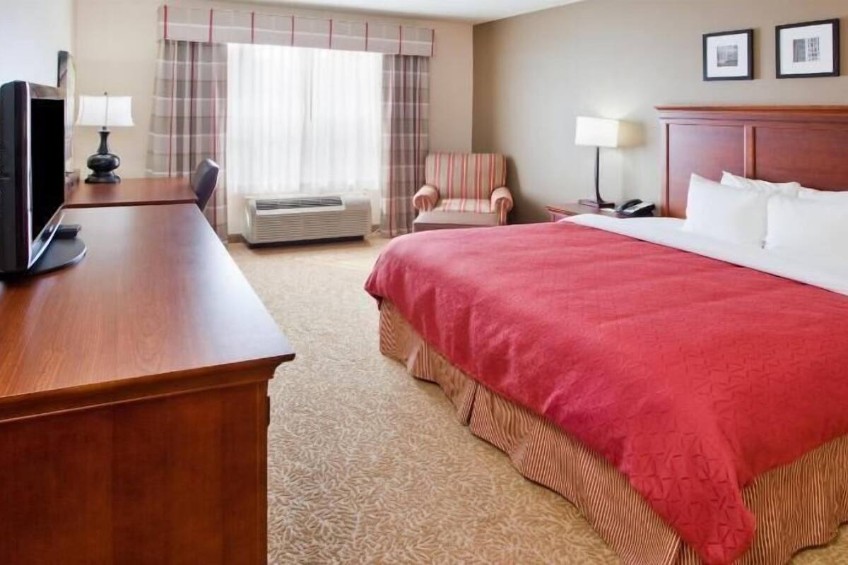 A hotel room with a large bed, a desk with a television, a chair, and a window with curtains.