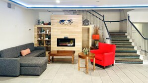 A living room with a grey sofa, a red armchair, a wooden TV stand, and a staircase with a patterned carpet. - Baymont Inn & Suites by Wyndham Morrow/Atlanta I-75 South (Morrow)